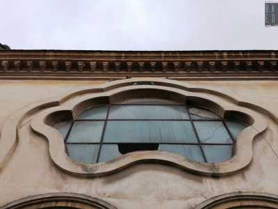 Ancora pi� in alto si fa notare un�apertura a vetri polilobata iscritta in una cornice in pietra. Chiude il prospetto un cornicione dentellato e un parapetto con elementi geometrici che corre lungo tutto il perimetro delimitando il terrazzo